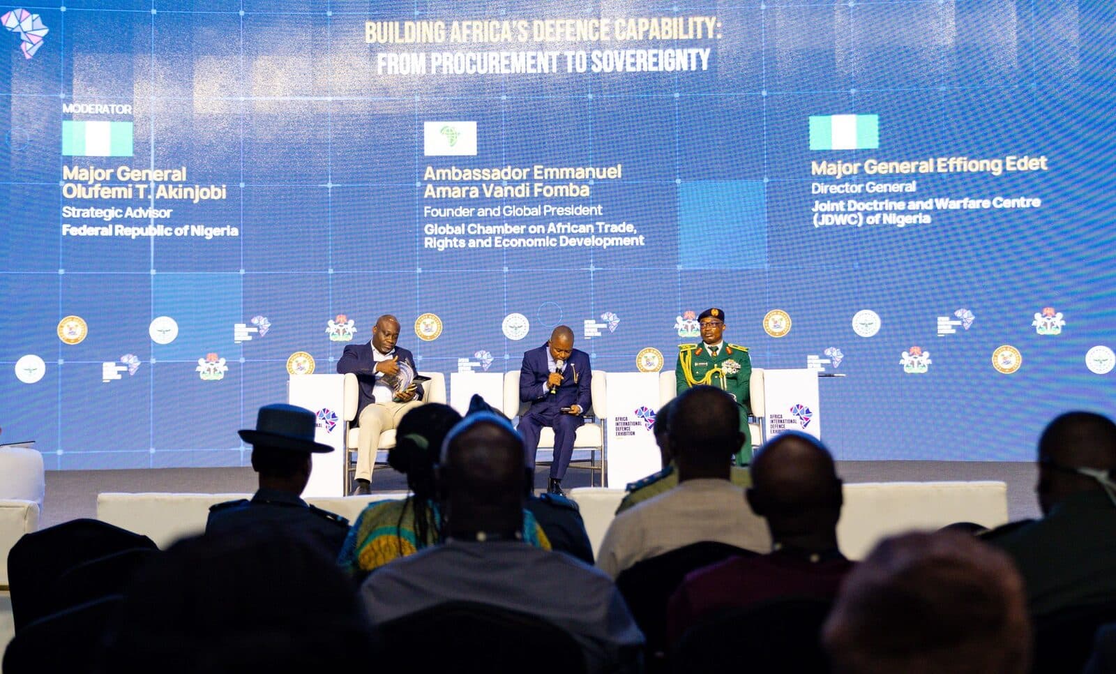 The Building Africa's Defence Capability panel on stage in the Plenary, with the speakers' names on the screen behind them.